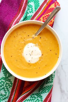 a white bowl filled with soup on top of a colorful table cloth next to a spoon