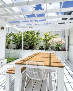 an outdoor dining area with wooden table and white wicker chairs under a pergolated roof