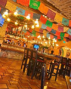 the interior of a restaurant with colorful flags hanging from the ceiling and tables in front of it