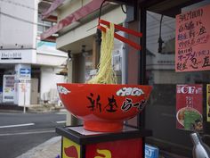 a red bowl with noodles in it sitting on top of a stand next to a street