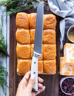 a person holding a knife near some breads and cranberries on a cutting board