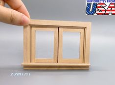 a hand holding a small wooden box with two windows on the front and back side