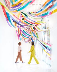 two people walking down a hallway with colorful streamers hanging from the ceiling