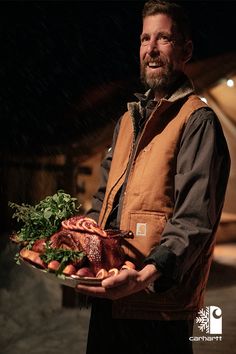 a man holding a platter full of meat and vegetables in the snow at night