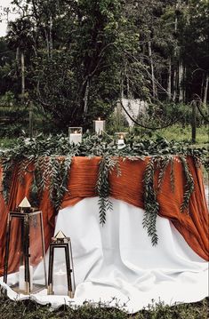 an orange and white cloth draped over the back of a table with two lanterns on it