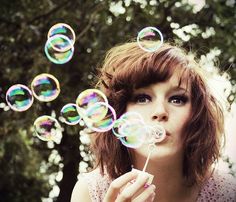 a woman blowing bubbles in the air with her eyes wide open and one eye closed