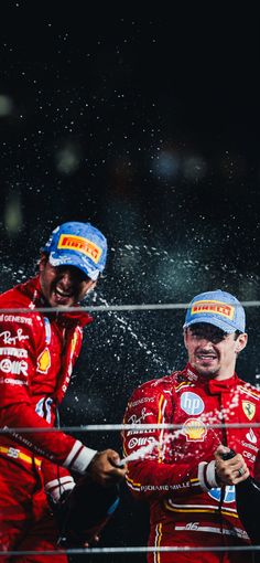 two men in red racing suits splash water on each other as they stand next to each other