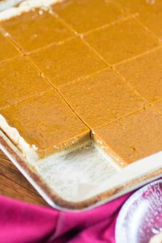 a pan filled with peanut butter squares on top of a wooden table next to a glass plate