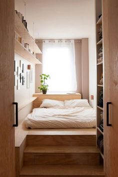 a bed sitting under a window in a bedroom next to a wooden shelf filled with books