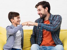 a man and boy sitting on a yellow couch arm wrestling each other's fists