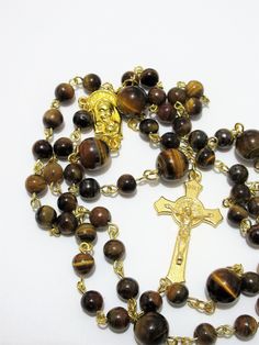 "This Tiger's eye Catholic rosary is made with Grade a gemstones. The hand turned links are gold plated as is the connector. The golden cross is from Italy. The rosary measures 26\" in the body and has a 5\" cross drop. This rosary will be slipped into a velvet bag and shipped in a bubble mailer." Gold Rosary Bracelet With Cross And 8mm Beads, Spiritual Gold Rosary With 8mm Beads, Gold Spiritual Rosary Bracelet With Polished Beads, Spiritual Yellow Gold Rosary With Round Beads, Brown Crucifix Necklace In Spiritual Style, Yellow Gold Rosary With Round Beads, Spiritual Brown Crucifix Necklace, Gold Spiritual Rosary With Cross, Gold Cross Rosary Spiritual