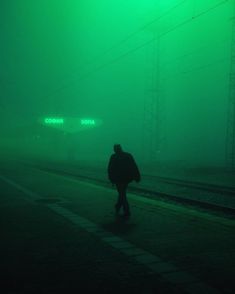 a person is walking on the train tracks in the foggy night with their back to the camera