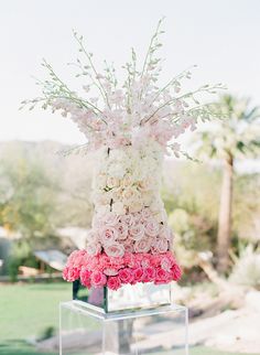 a vase filled with pink and white flowers on top of a glass stand in the grass