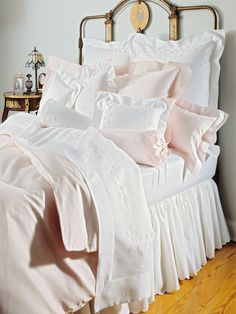 a bed with white ruffled sheets and pink pillows