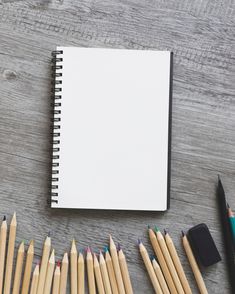 several pencils are lined up next to an open notebook on a wooden table with erasers