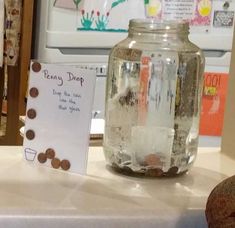 a glass jar with coins in it sitting on a table next to a sign that says penny deep