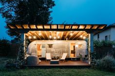 an outdoor covered patio with chairs and lights on it's roof, surrounded by greenery