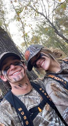 two people with face paint standing next to each other in front of a large tree