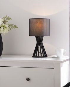 a table lamp sitting on top of a white dresser next to a vase with flowers