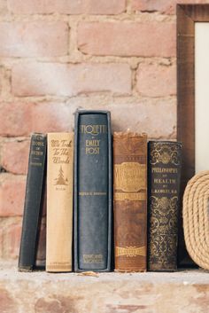 several books are lined up on a shelf next to a rope and wood frame in front of a brick wall