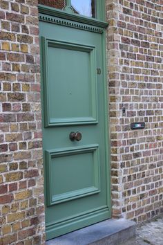 a green door on the side of a brick building with a cat sitting in front of it