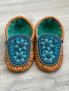 a pair of brown shoes with blue embroidered flowers on them sitting on top of a wooden floor