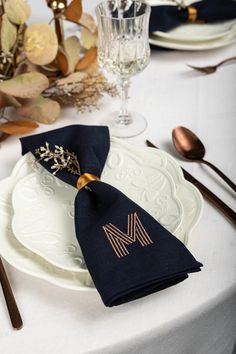 a white plate topped with a black napkin next to a gold monogrammed napkin