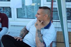 a man with tattoos on his arm sitting in front of a building