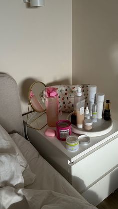 an assortment of beauty products sitting on top of a white dresser next to a bed