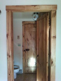 an open door leading to a bathroom with a toilet in the corner and wood paneling on the walls