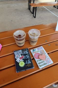 two cups of ice cream sitting on top of a wooden bench next to a book