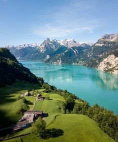 an aerial view of a lake surrounded by mountains and green grass with houses on the shore