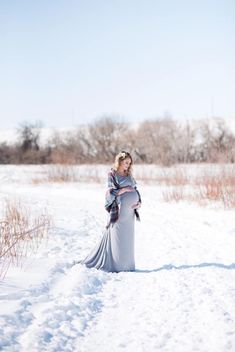 a pregnant woman standing in the snow with her belly wrapped around her waist and wearing a plaid blanket