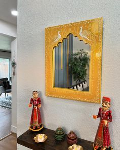 two figurines sitting on top of a wooden table in front of a mirror