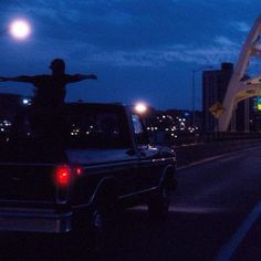 a man standing on the back of a truck in front of a bridge at night