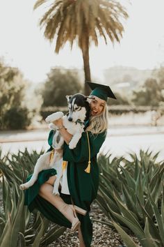 a woman in graduation gown holding a husky dog and smiling at the camera with palm trees behind her