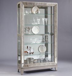 a silver and glass display case with dishes on it's sides, in front of a gray background