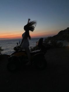 a woman riding an atv on top of a hill next to the ocean at sunset