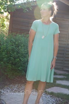 a woman standing in front of a wooden building wearing a green dress and white shoes