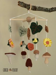 a crocheted mobile hanging from a tree branch with leaves and mushrooms on it