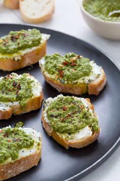 four pieces of bread with pesto on them and two bowls of garlic bread in the background