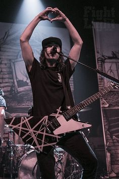 a man standing on stage with his hands in the air while holding up a guitar