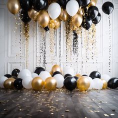 balloons and streamers are hanging from the ceiling in front of a white wall with black and gold confetti