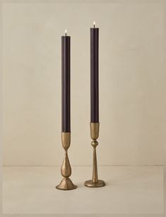 two tall candles sitting next to each other on top of a white table with one candle in the middle