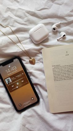 an open book, headphones and earbuds on a bed next to an iphone