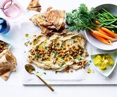 an assortment of food is displayed on a white table with bowls and spoons next to it