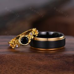 two wedding rings sitting on top of a wooden table next to each other, one with a black diamond in the middle