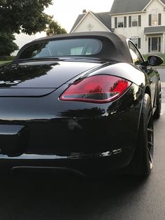 the back end of a black sports car parked in front of a large white house