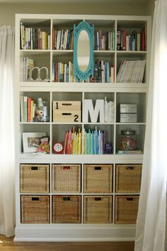 a bookshelf filled with lots of books next to a white curtain and window