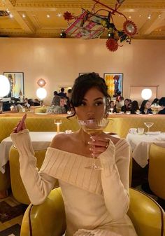 a woman sitting in a yellow chair holding a wine glass up to her face with both hands